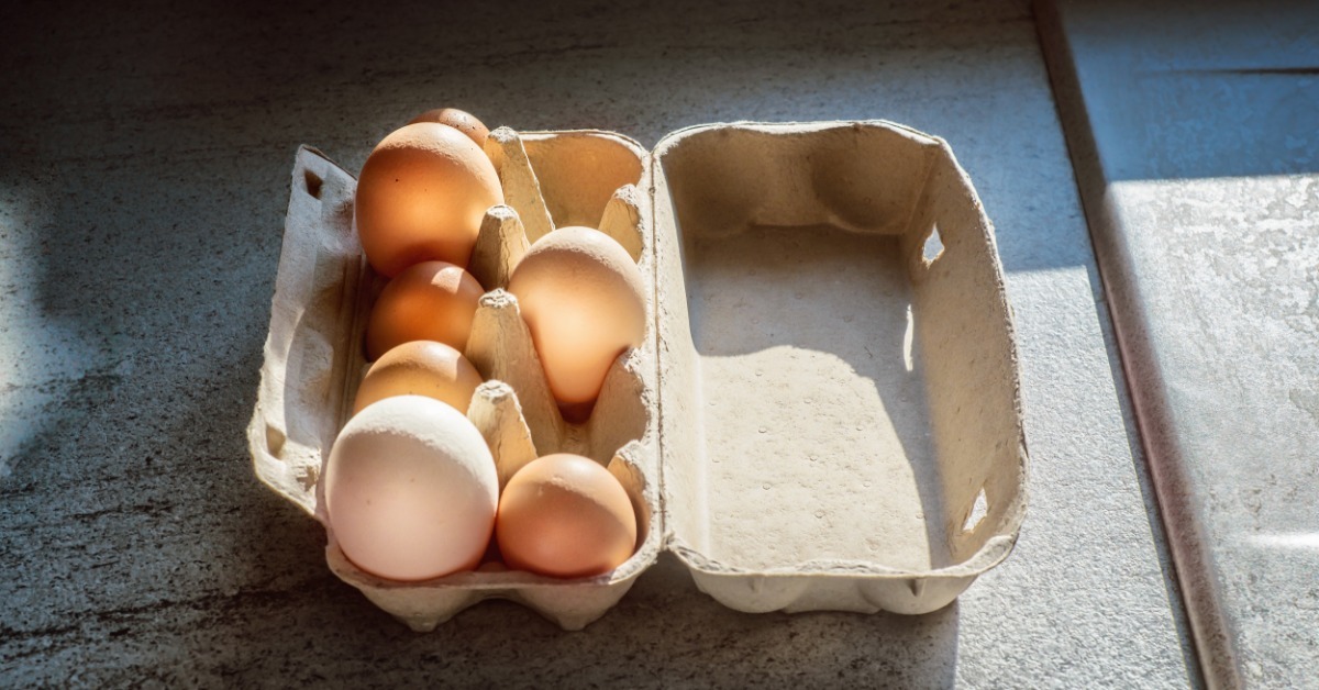 A close-up of brown and white eggs of different sizes arranged in a cardboard carton on a wooden table.